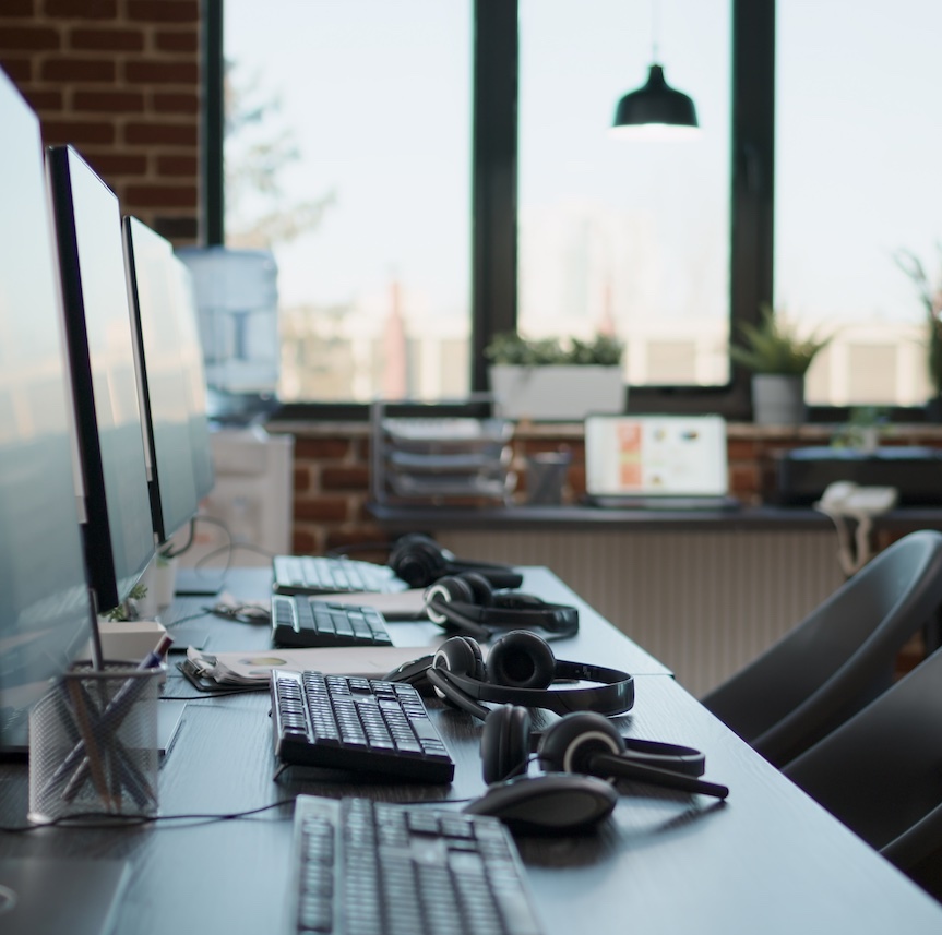 No people at desk with multiple computers in call center office, used by telemarketing agents to answer phone calls on helpline. Empty space with technology to give assistance at customer care.